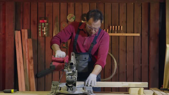 Man Carpenter Cuts a Wooden Beam with a Circular Saw in the Workshop.