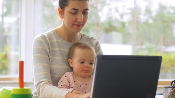 Mother with Baby Working on Laptop at Home Office
