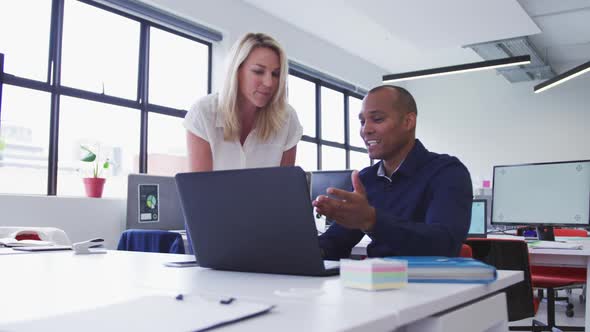 Diverse business colleagues talking at desk using laptop in office