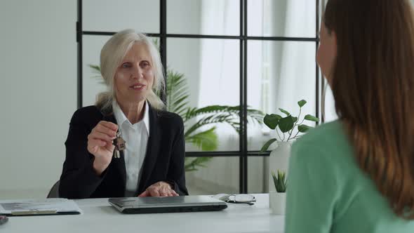 Elderly Female Real Estate Agent Hands Over the Keys to an Apartment to a Female Client