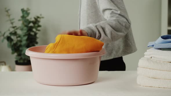 Woman Putting Dirty Clothes Into Basin on Iron Board Closeup Preparing for Washing