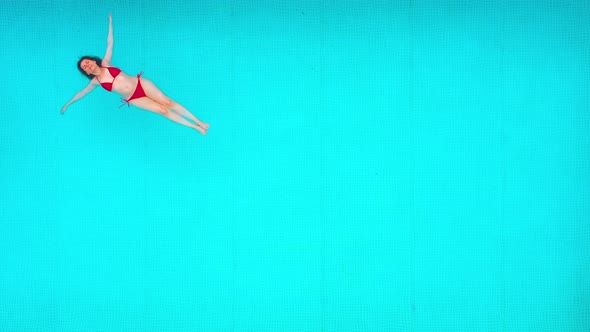 View From the Top As a Woman in Red Swimsuit Lying on Her Back in the Pool