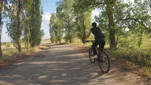 A Young Girl Rides a Bicycle Along a Forest Road.