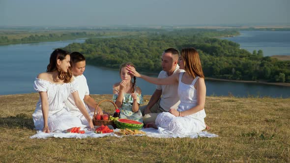 Happy Family with Children Has Picnic on Hilly Riverbank