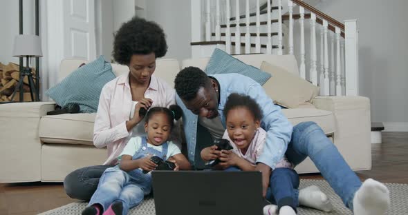 African American Couple with Their Two Small Daughters Sitting on the Floor and Playing Videogame 