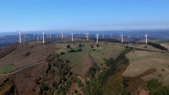 Wind farm with wind turbines moving the helices in the mountains with forests of green trees on a su