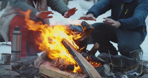 Friends Camping in Winter Forest Warming Hands By Fire