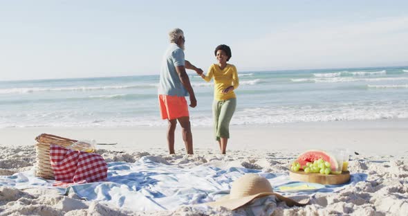 Happy african american couple having picnic and dancing on sunny beach