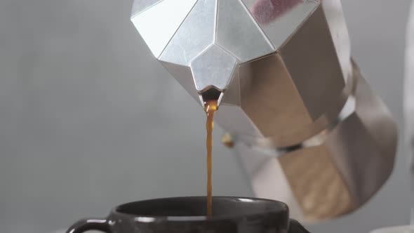 Rack Focus Close Up View of Pouring Coffee From Shiny Geyser Coffee Maker Into Black Cup