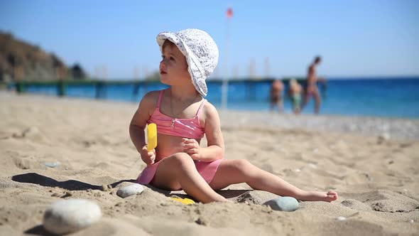 Little Girl in Pink Swimsuit Playing with Sand on the Beach