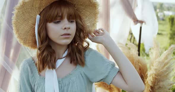 Close Up of Teen Girl in Straw Hat and Summer Clothes Posings on Green Field Landscape in