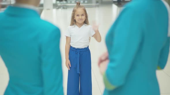 Portrait of Cute Little Caucasian Girl Waving To Unrecognizable Stewardesses in Airport. Pretty