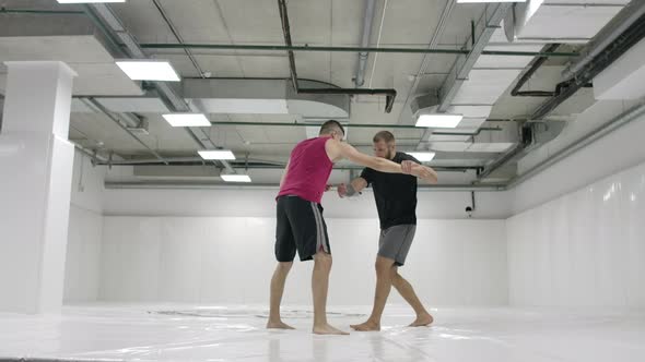 Two Male Wrestlers in a White Room Work Out Throwing Mats