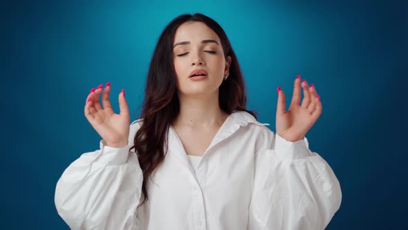 Stressed Young Woman Tries to Calm Down Breathing Deeply Against Blue Background