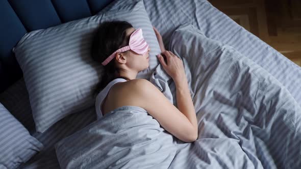 Woman in a Pink Eye Mask Lies Under a Blanket in a Bed and Suffers From Insomnia