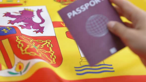 Hand Putting Red Passport on Spanish Flag Background, Illegal Immigration