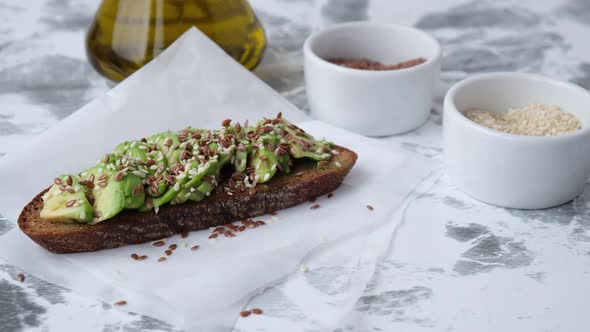 Female hand making Healthy avocado toast on wooden board. Sesame and flax seeds. Vegetarian food.