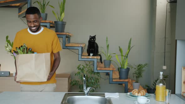 Cheerful Guy Bringing Paper Bag with Food to Kitchen Unpacking Groceries Smiling