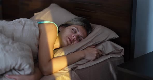 Happy Woman Wakes Up in Morning From Bright Sunbeam in Bedroom