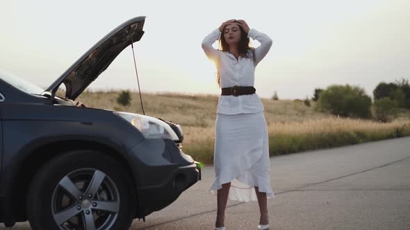 View of Nervous Woman Perplexing Not to Stand and Looks Under Hood Out of City