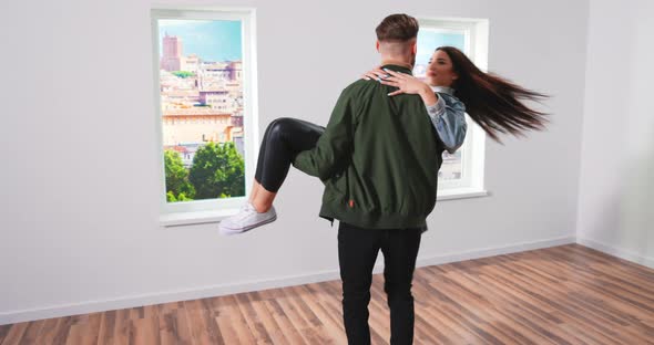 Happy Young Couple in Their Newly Purchased Rented Apartment Boyfriend Carries His Girlfriend Spins