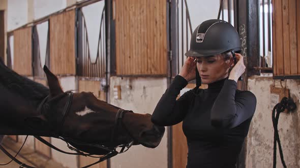 A Horsewoman Puts on a Plastic Helmet Standing Near the Horse