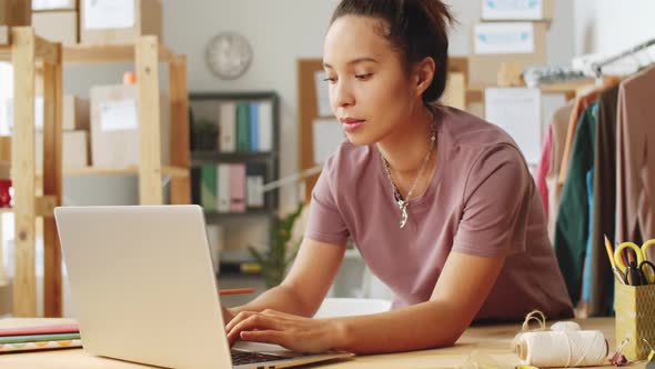 Mixed-Race Woman Working on Laptop in Office of Clothes Shop