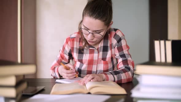The girl with glasses is engaged in training, sitting at a table with books