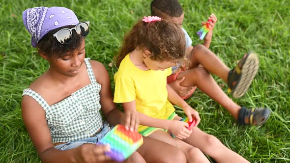 Children of Different Races Sit on the Grass and Play with an Antistress Toy Popit