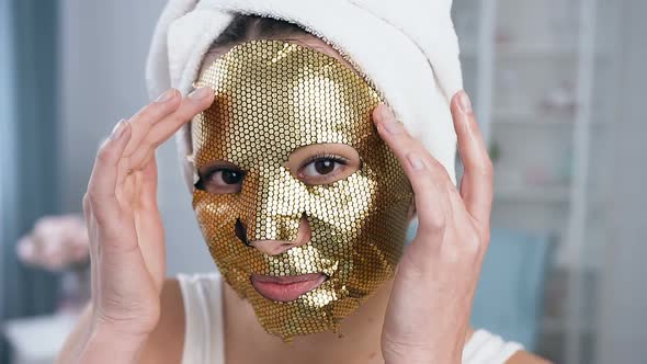 Smiling Woman Fixing Rejuvenating Cosmetic Golden Tissue Mask on Face