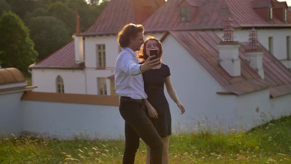 Couple Takes a Selfie Against with the Gatchina's Priory Palace in a Park