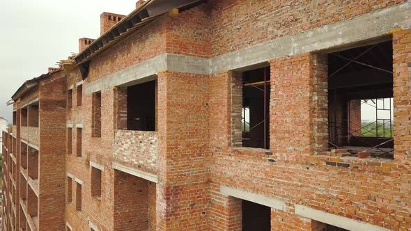 Aerial view of unfinished brick apartment building with wooden roof structure under construction.