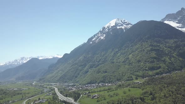 Aerial drone shot of a valley with roads and towns underneath snow covered mountains in Lavey Les Ba