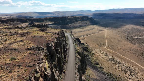 Aerial shot following a highway carved into the mountainside in the desert.