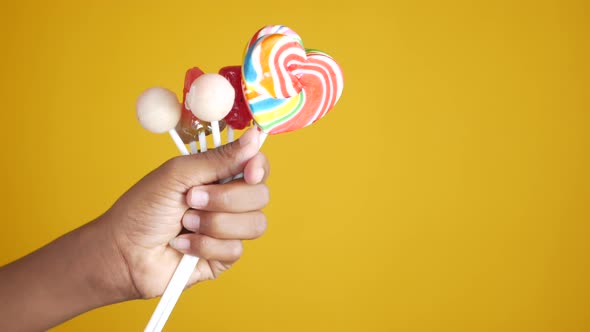 Hand Holding Lollipop Candy on Yellow Background