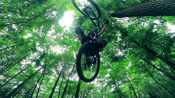 Downside View of a Man Jumping on a Bike in the Forest