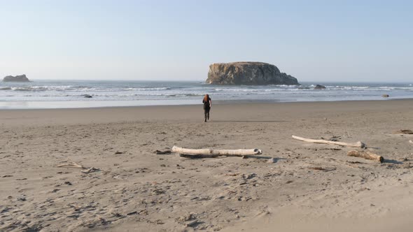 A man with long red hair runs down a beach towards the water.