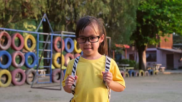 Cute smiling schoolgirl in summer clothes with a backpack standing at school.