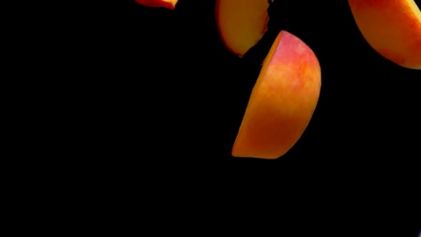 Closeup of Halves of Ripe Apricots Falling Diagonally on a Black Background