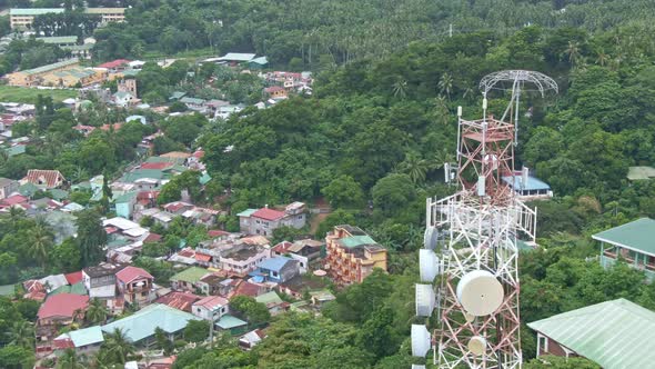 Aerial drone view of signal tower, houses and buildings surrounded by trees from Puerto Galera, Phil