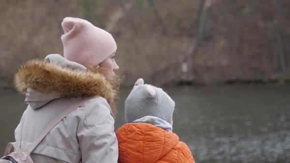 A Mother and Little Daughter Sit on the Bank of the River on the Bench and Talk Later in the Fall