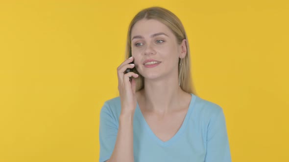 Young Woman Talking on Phone on Yellow Background