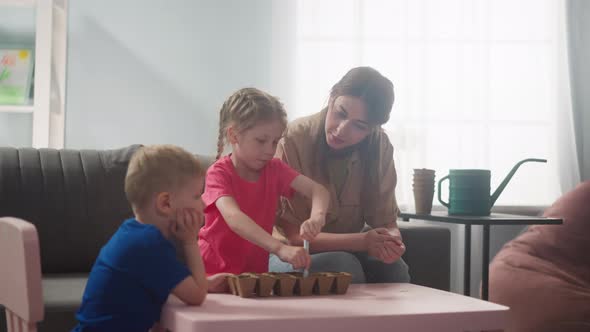 Girl Digs Holes in Soil with Mother and Brother at Home