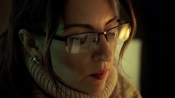 Pretty woman in eyeglasses late at night scrolling with smartphone