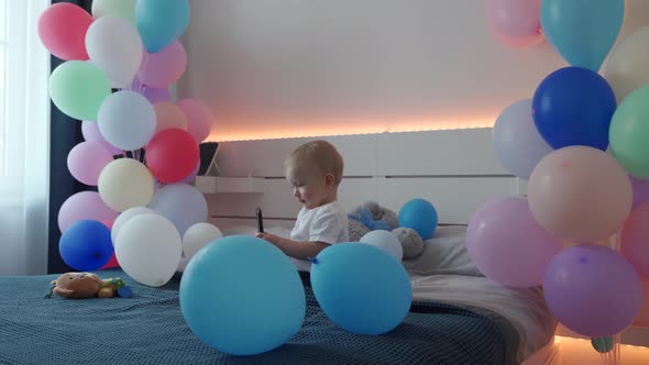 Cute Small Child Playing with Smartphone on Bed in Bedroom Decorated with Colorful Balloons 1 Year