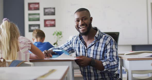 Video of happy african american male teacher helping pupils during lessons