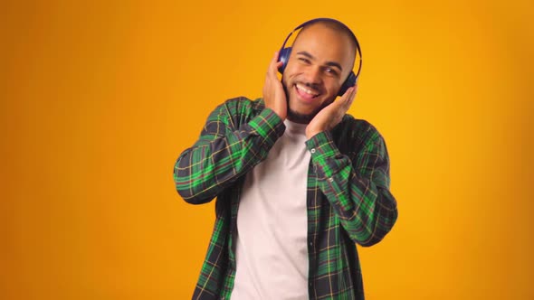 Handsome Joyful African American Man Listening to Music with Headphones Against Yellow Background