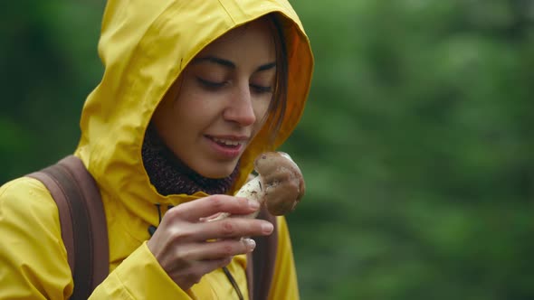 Joyful Woman in Yellow Raincoat Sniffing a Big a Mushroom Boletus in Green Thickets in Wet Wood