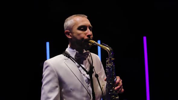 Camera Rotates Around Stylish Man in a White Suit with a Bow Tie Plays the Saxophone