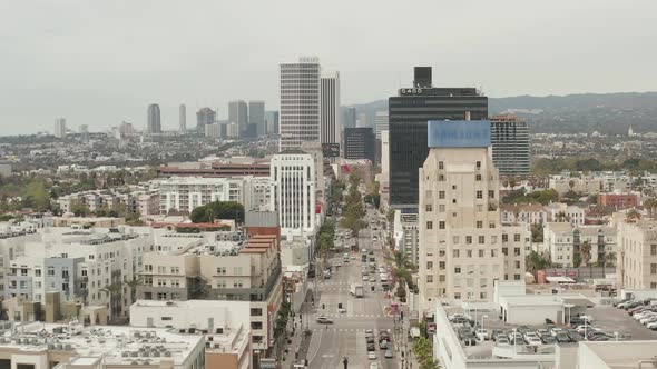 AERIAL: Flight Over Wilshire Boulevard Close To Street and Buildings with Car Traffic in Los Angeles